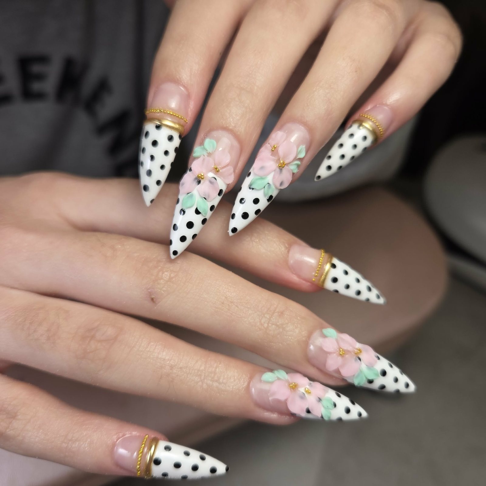 Lange stiletto nagels met zwarte stippen, roze bloemen en een gouden randje